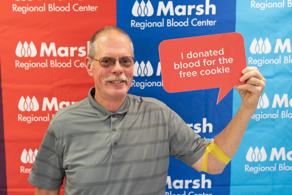 Smiling man holds sign that says "I donated blood for the free cookie"