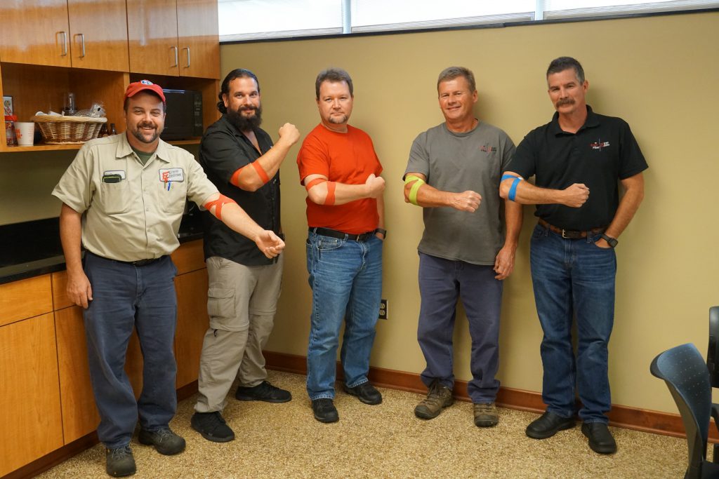 Five men flex their arms to show their bandages after giving blood