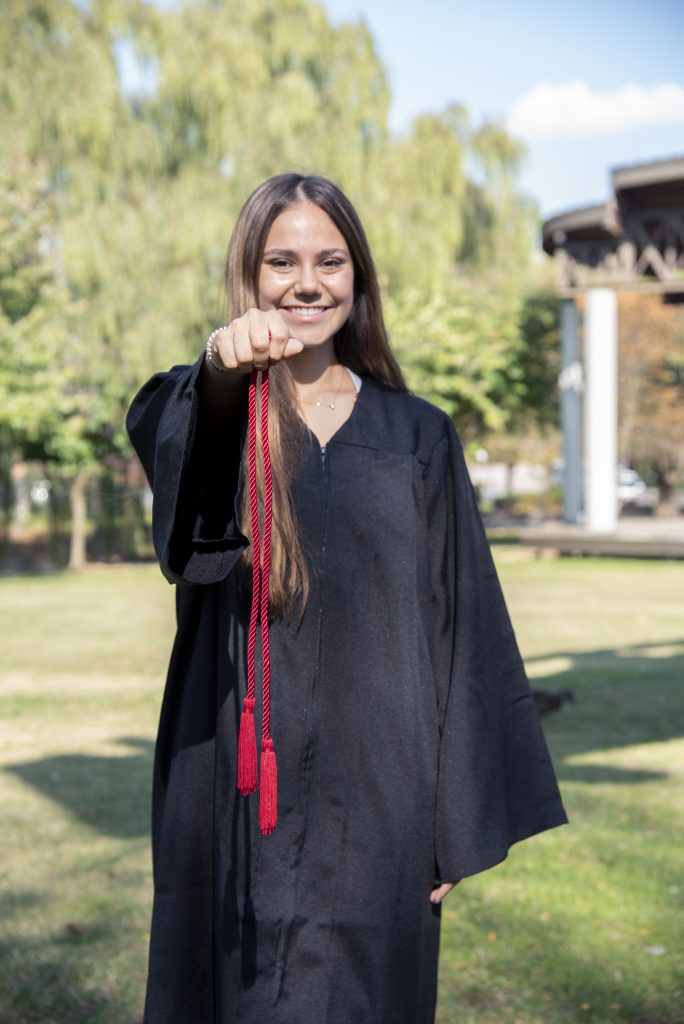 High School girl wearing regalia holds red cord proudly