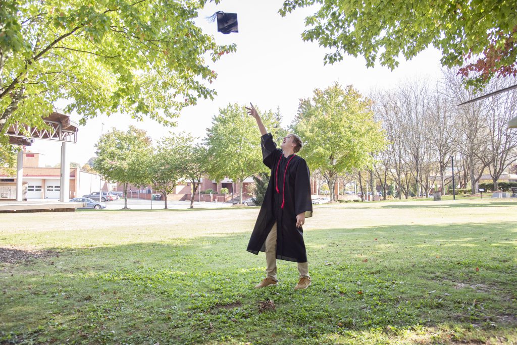 High school graduate tosses cap in the air and wears red cord from being a loyal blood donor