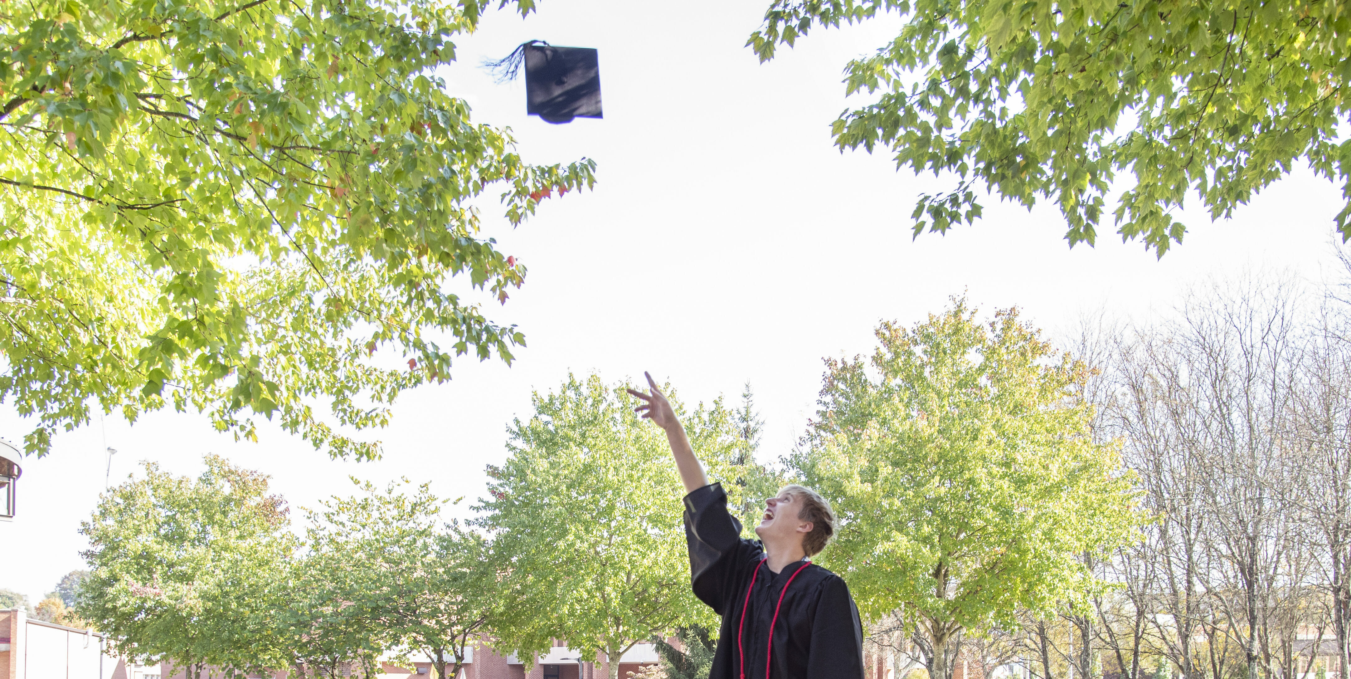 High school graduate tosses cap in the air and wears red cord from being a loyal blood donor