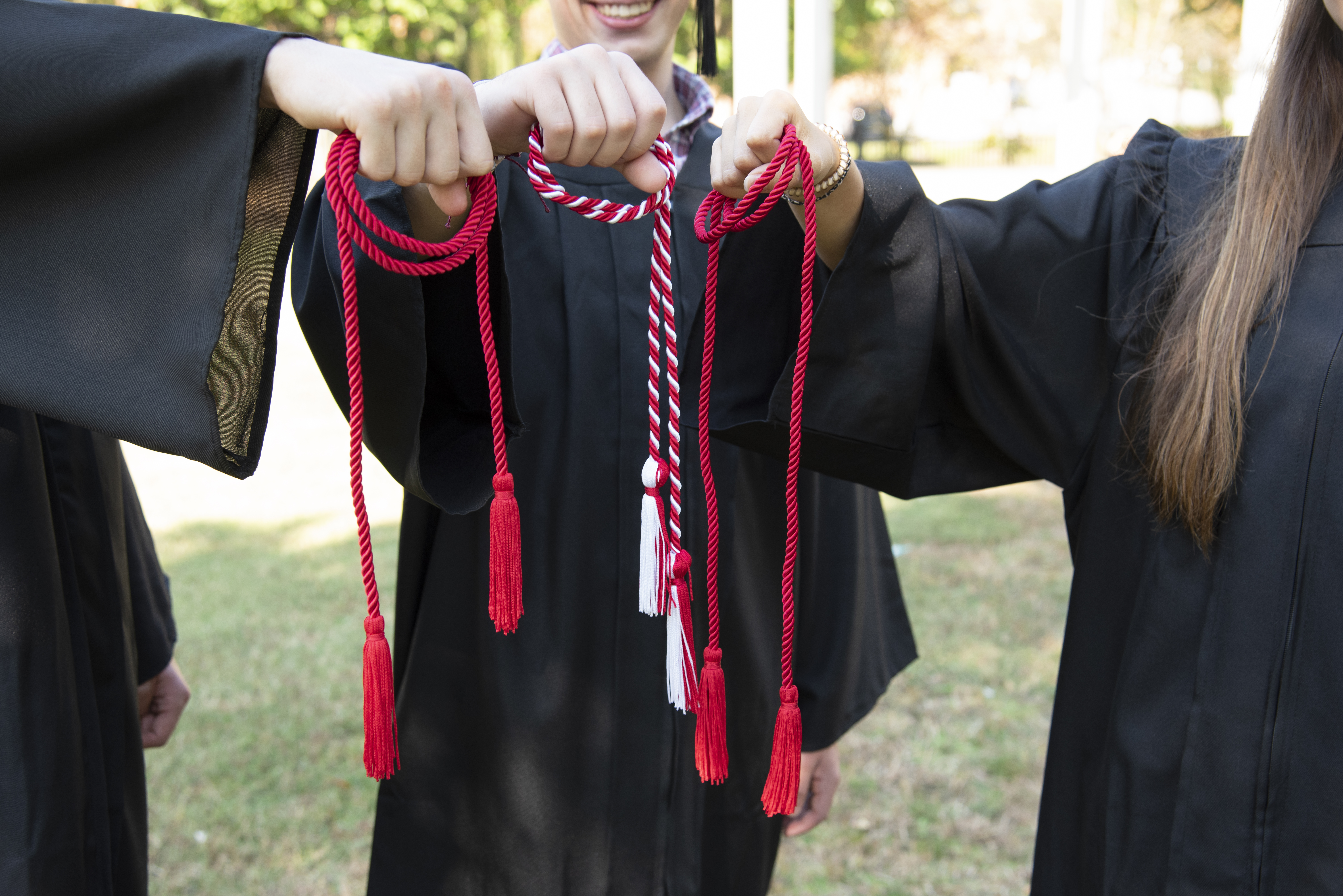 Three hands holding red cords for graduation